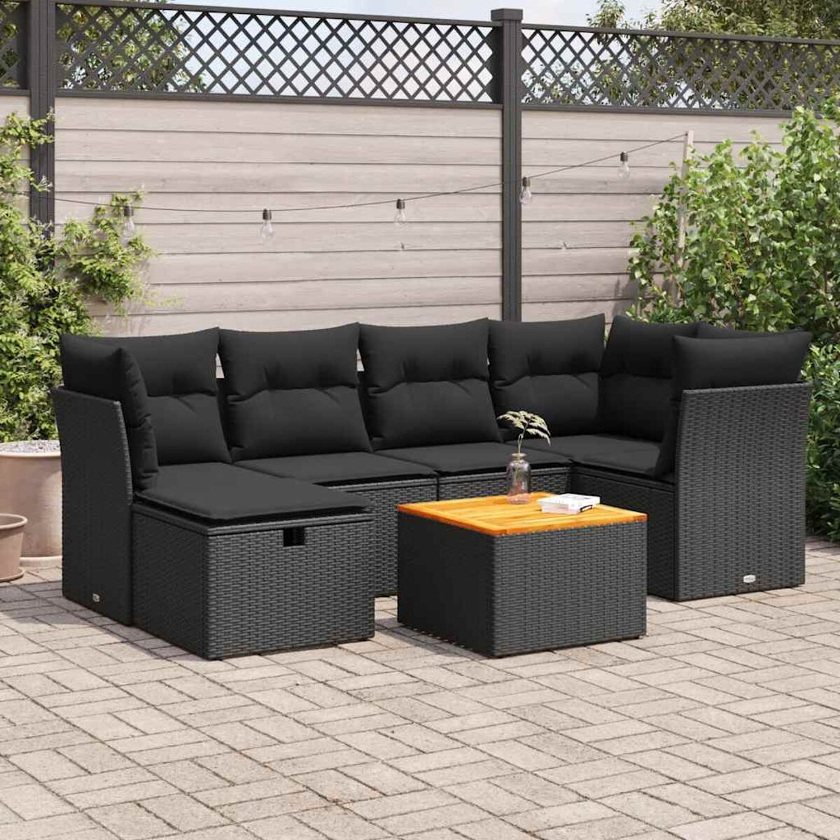 Set divano esterno in vimini nero con cuscini neri, tavolo in legno e vano contenitore quadrato.