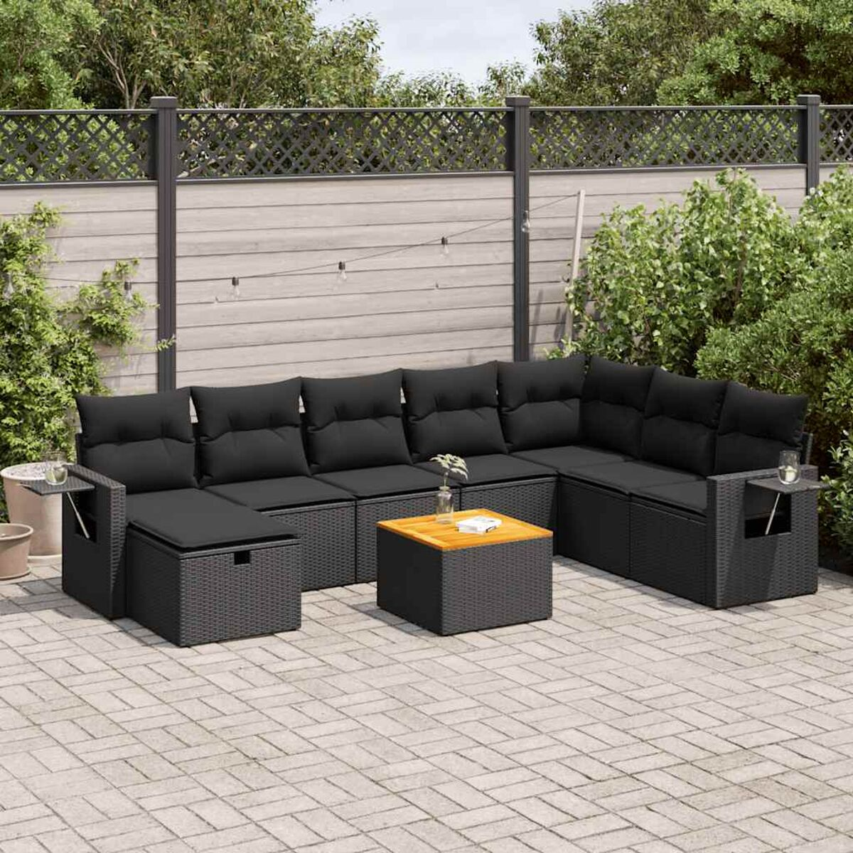 Set divano in rattan nero da esterno con cuscini neri e tavolo in legno.