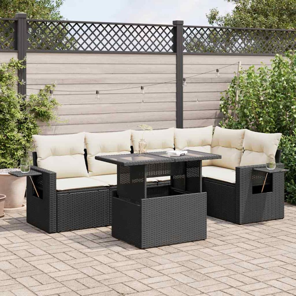Set di mobili da esterno in rattan nero con cuscini beige e tavolo elevabile. Sfondo: recinzione e piante.