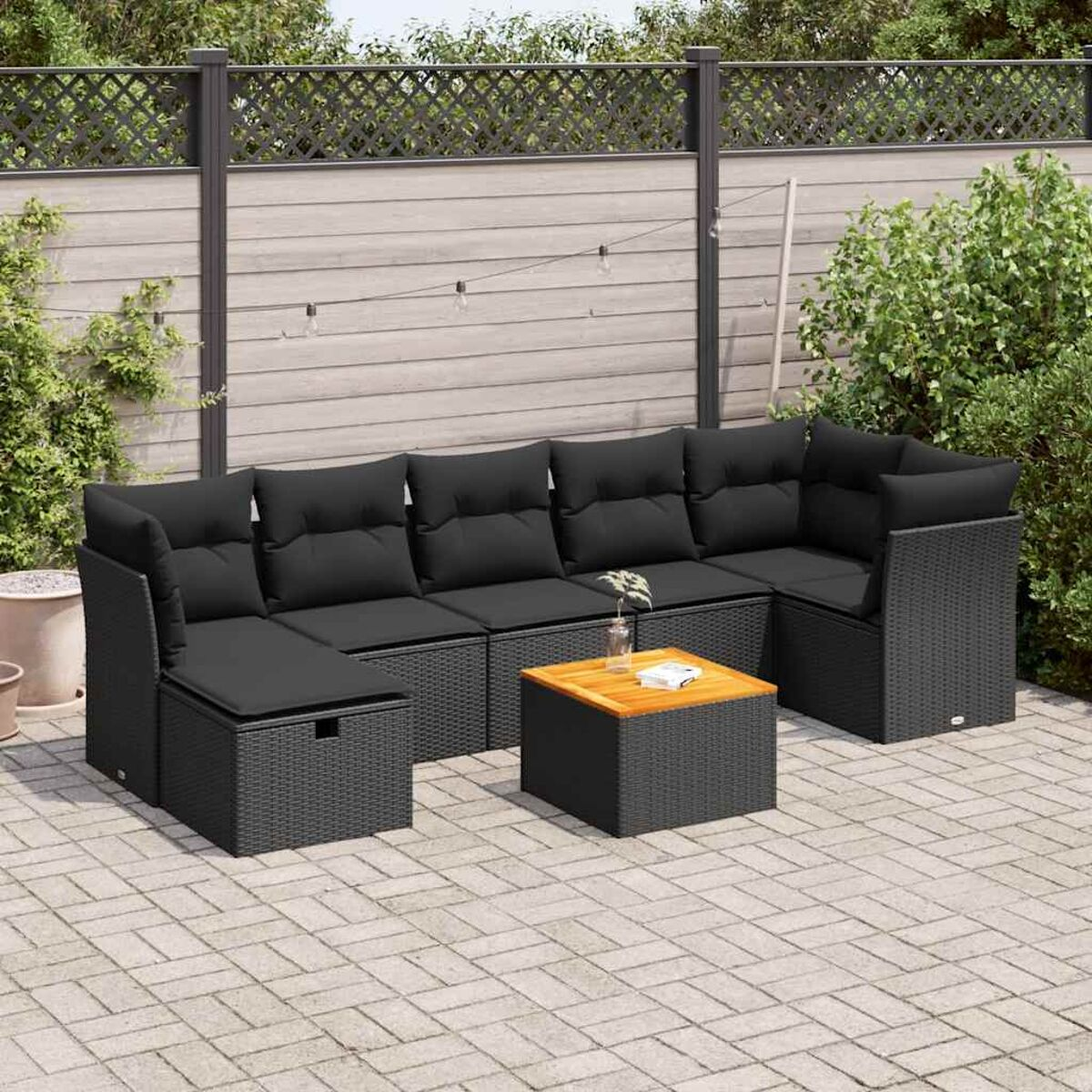 Set di mobili da esterno in rattan nero con cuscini neri. Include un divano componibile, un tavolino e un pouf.
