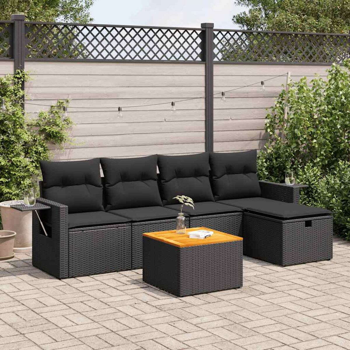 Schwarzes Outdoor-Ecksofa mit Holztisch. Die Szene ist eine Ziegelterrasse, umgeben von Grün.
