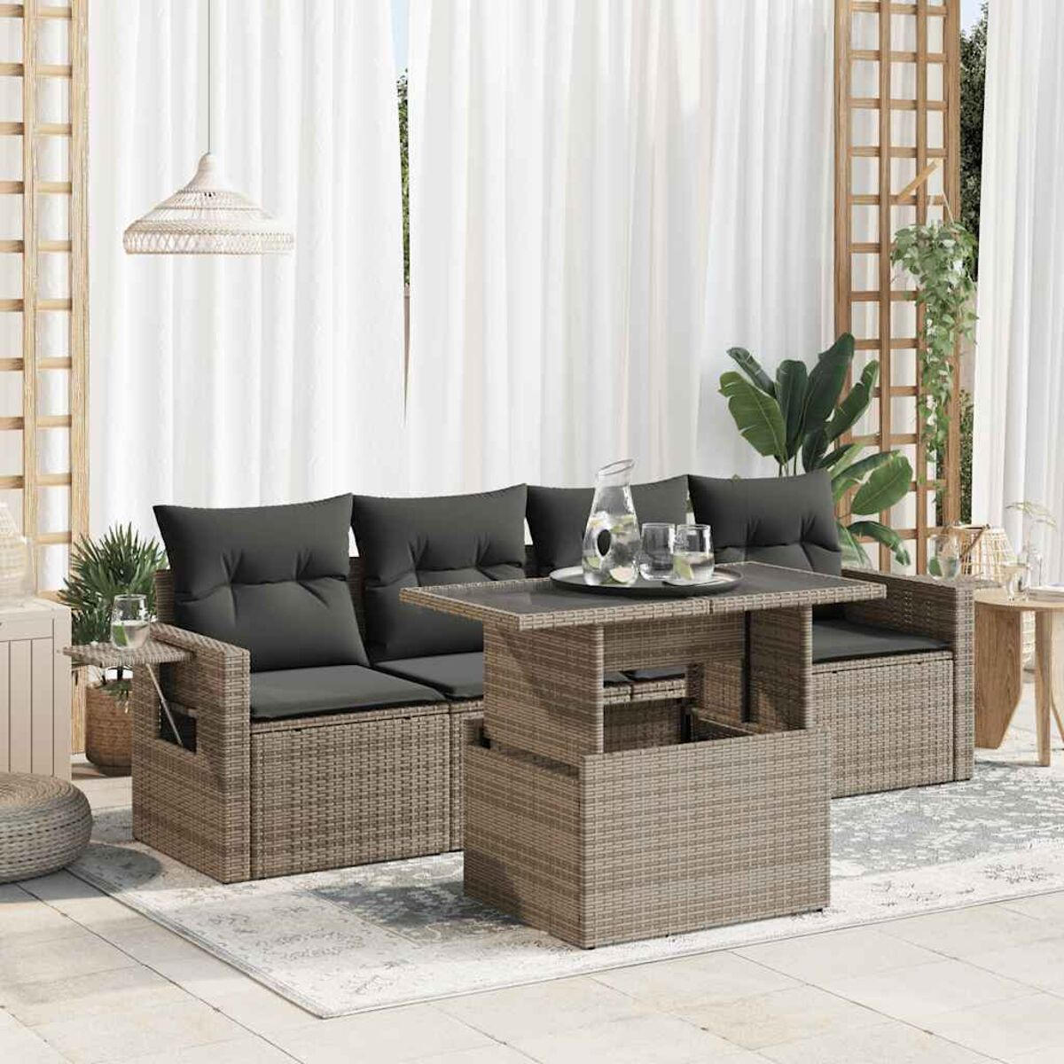 Garnitur für draußen mit Tisch, Sofas und Teppich. Die Möbel sind aus Rattan mit dunkelgrauen Kissen.