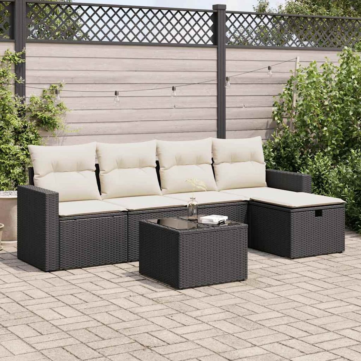 Rattan-Sofa im Freien mit cremefarbenen Kissen, einem Couchtisch und einem Aufbewahrungs-Hocker auf einer Terrasse.