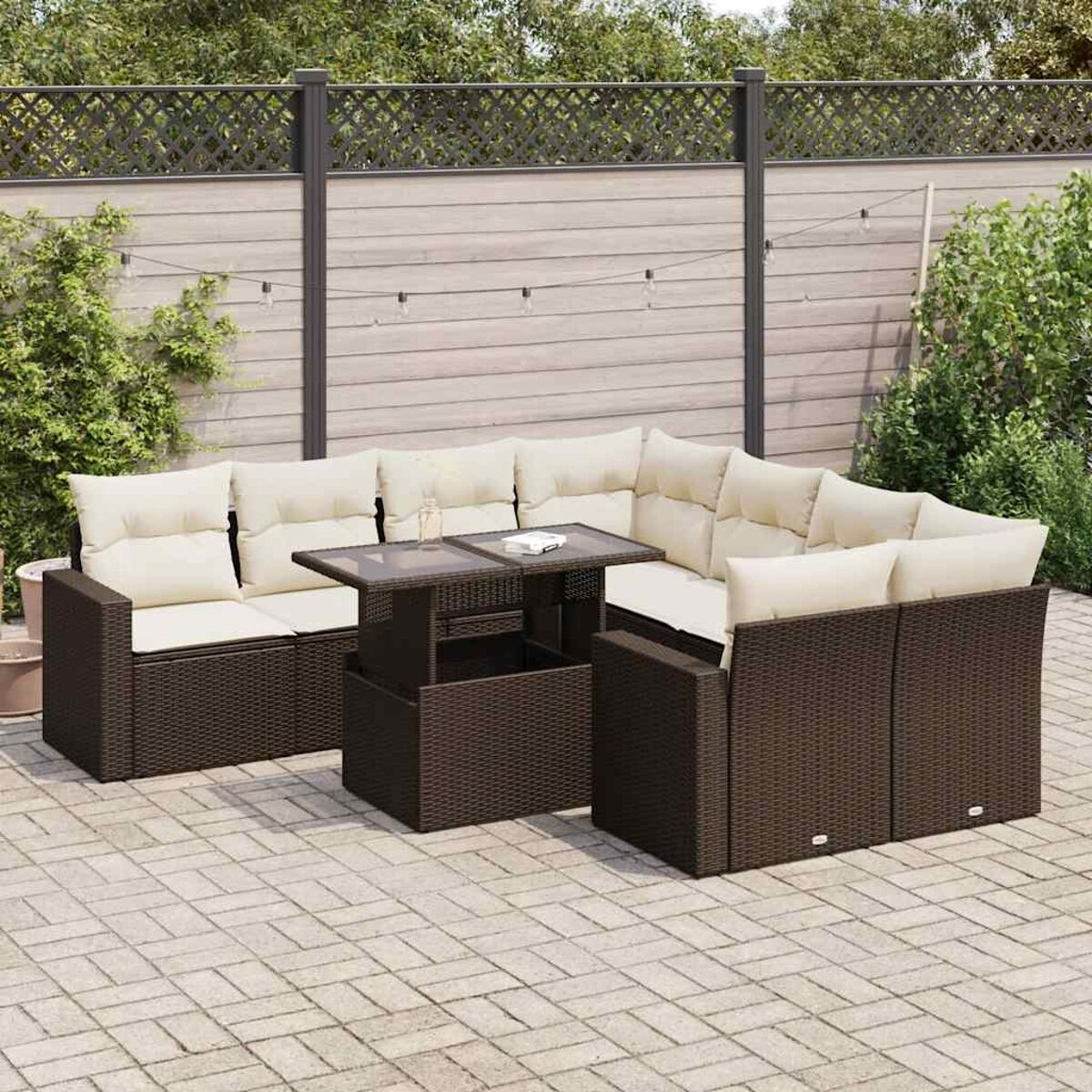 Braunes Outdoor-Ecksofa aus Korbgeflecht mit beigefarbenen Kissen und Tisch auf Backstein-Terrasse. Holzzaun.