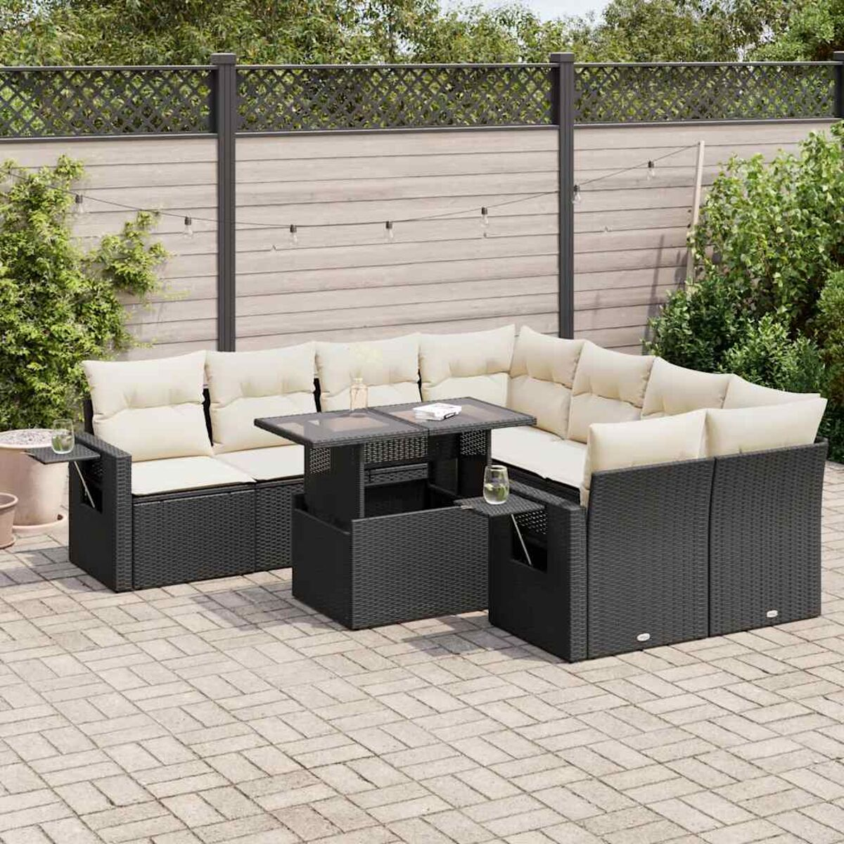 Divano angolare da esterno in rattan nero con cuscini color crema, un tavolo e una recinzione in legno in giardino.
