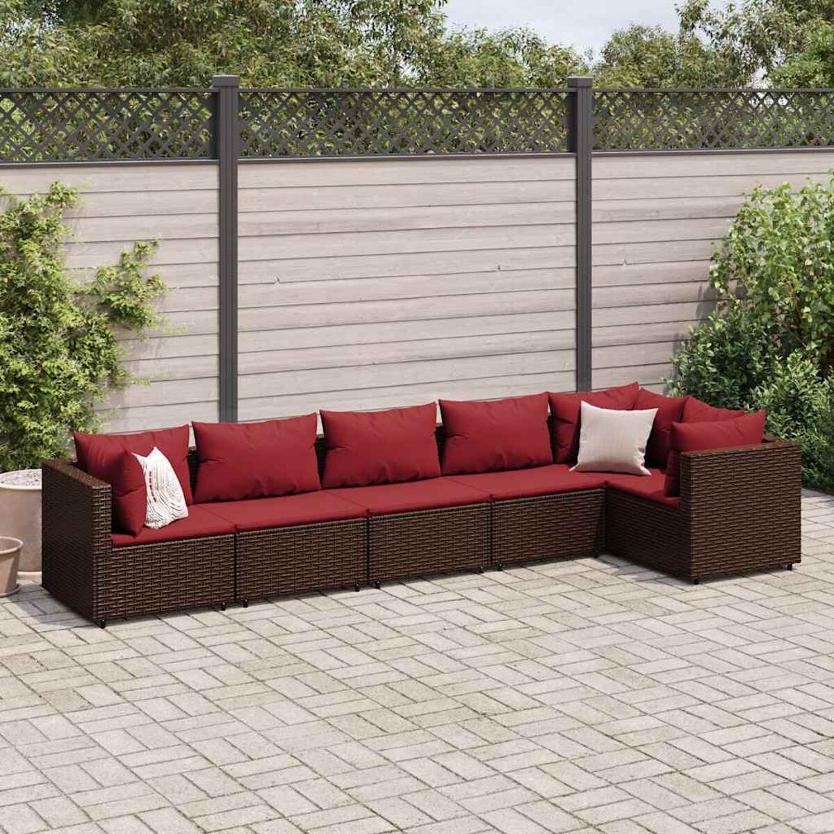 Set divano ad L in rattan marrone con cuscini rossi su un patio in mattoni.