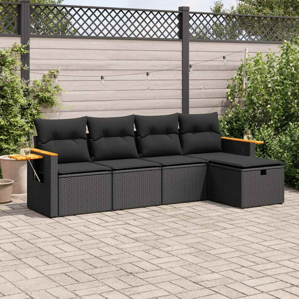 Set da esterno in vimini nero: divano e tavolino. Cuscini neri, braccioli in legno.