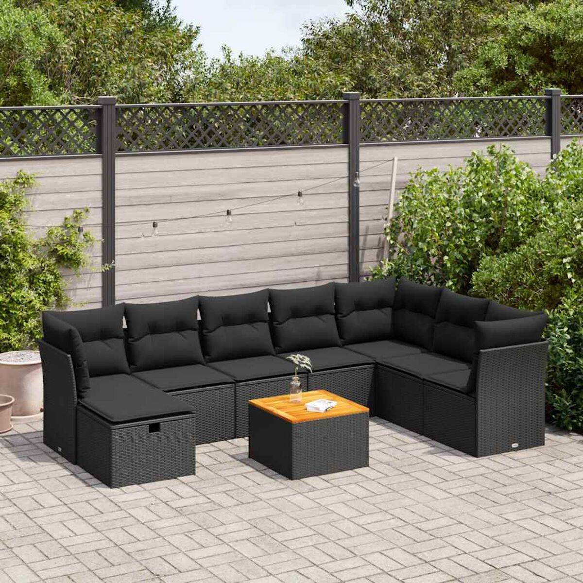 Schwarzes Rattan-Außensofa mit schwarzen Kissen, Holztisch auf einer Terrasse.