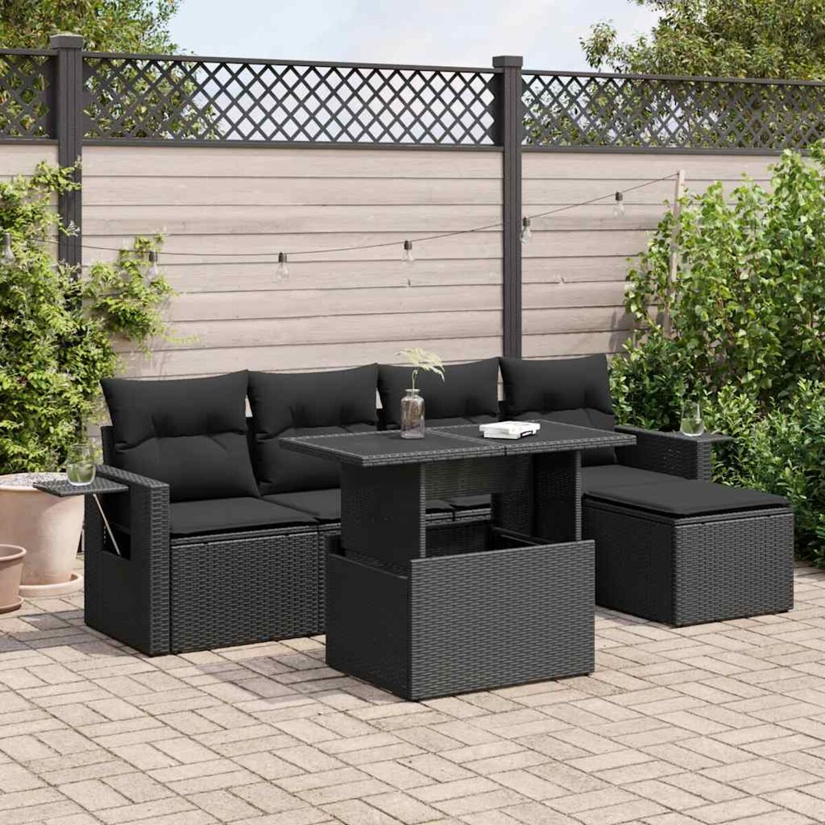 Sofá negro para exteriores con cojines negros. Mesa negra. Patio de ladrillo y plantas en el fondo. Cielo despejado.
