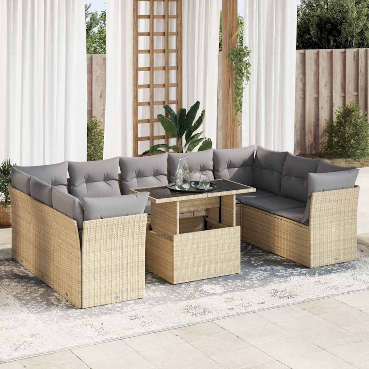 Juego de patio exterior con muebles de mimbre claros, cojines grises y una mesa de madera. Cortinas blancas al fondo.