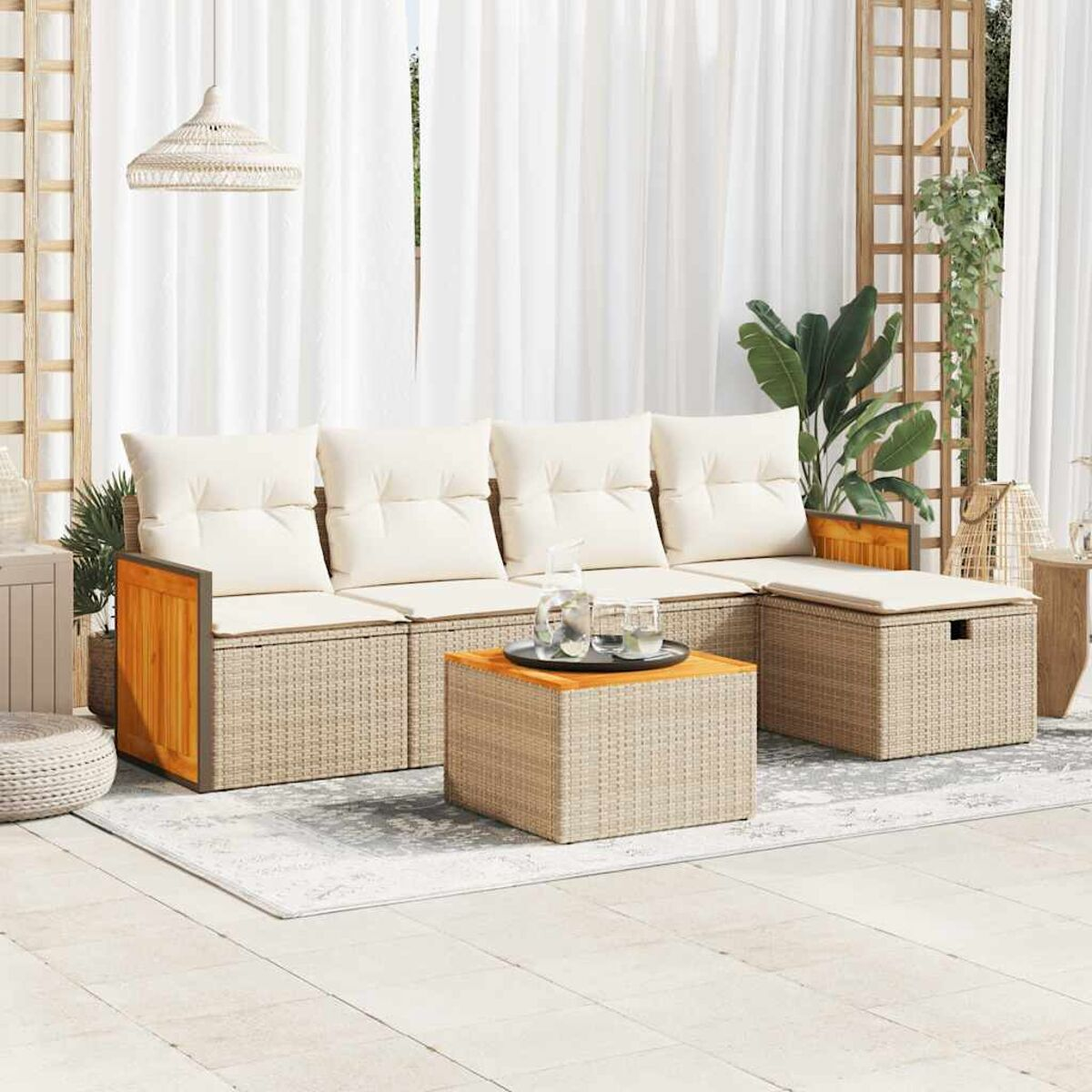Set divano in rattan da esterno con cuscini color crema e un tavolo in legno. Uno sfondo di tenda bianca.