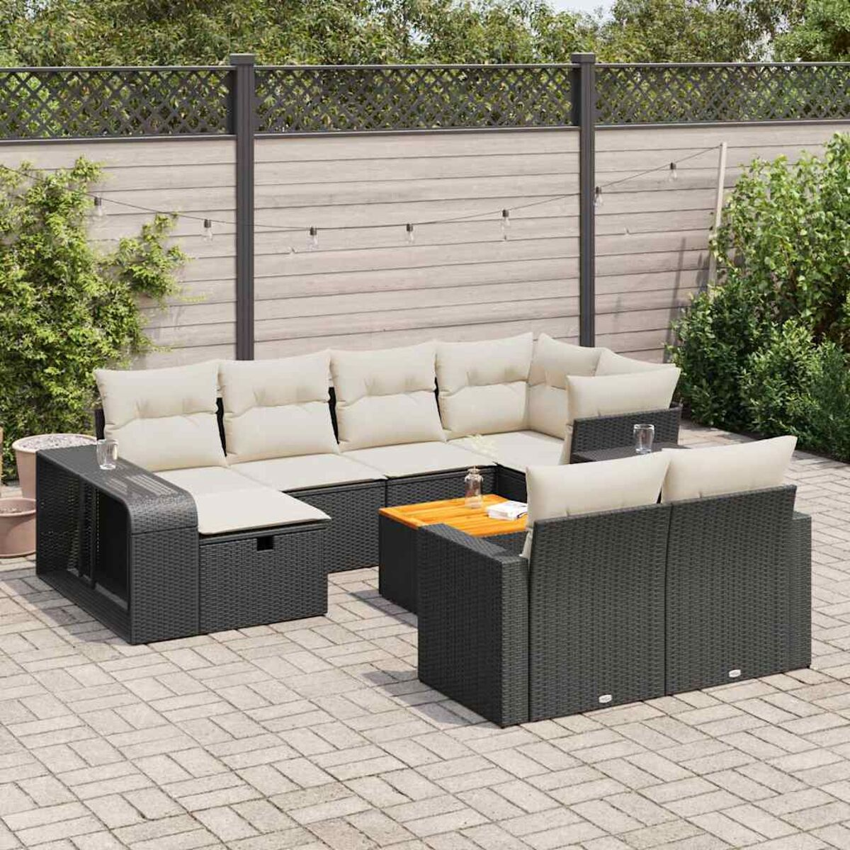 Schwarzes Outdoor-Möbelset aus Korbgeflecht mit cremefarbenen Kissen. Auf einer Backstein-Terrasse aufgestellt. Zaun.