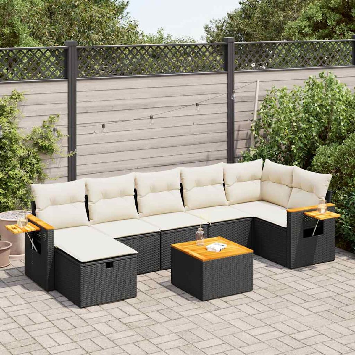 Schwarzes Rattan-Sofa-Set für den Außenbereich mit weißen Kissen. Enthält einen Tisch. Grüne Pflanzen und ein Zaun im Hintergrund.