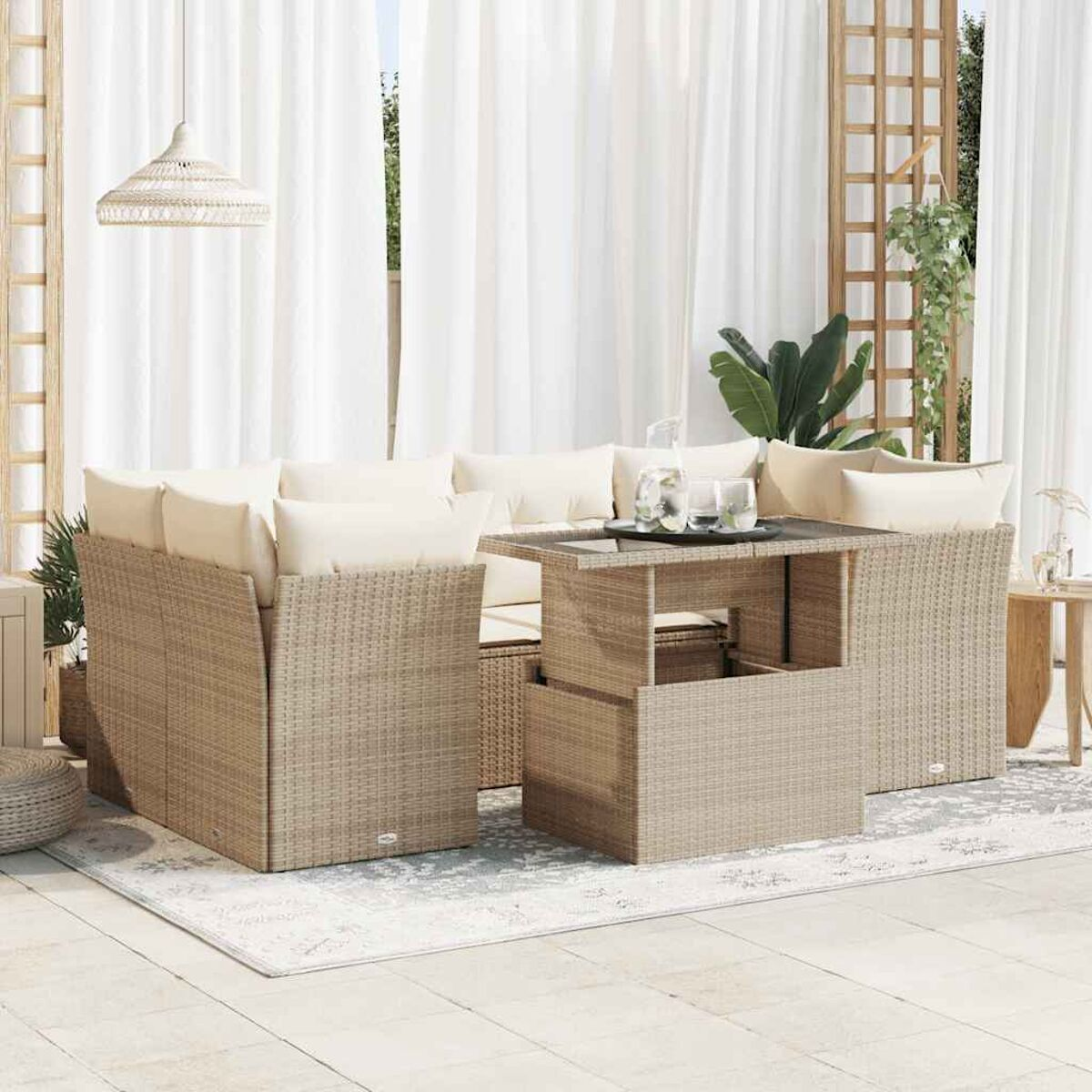 Set divani in rattan da esterno con cuscini, tavolo e tende bianche sullo sfondo.