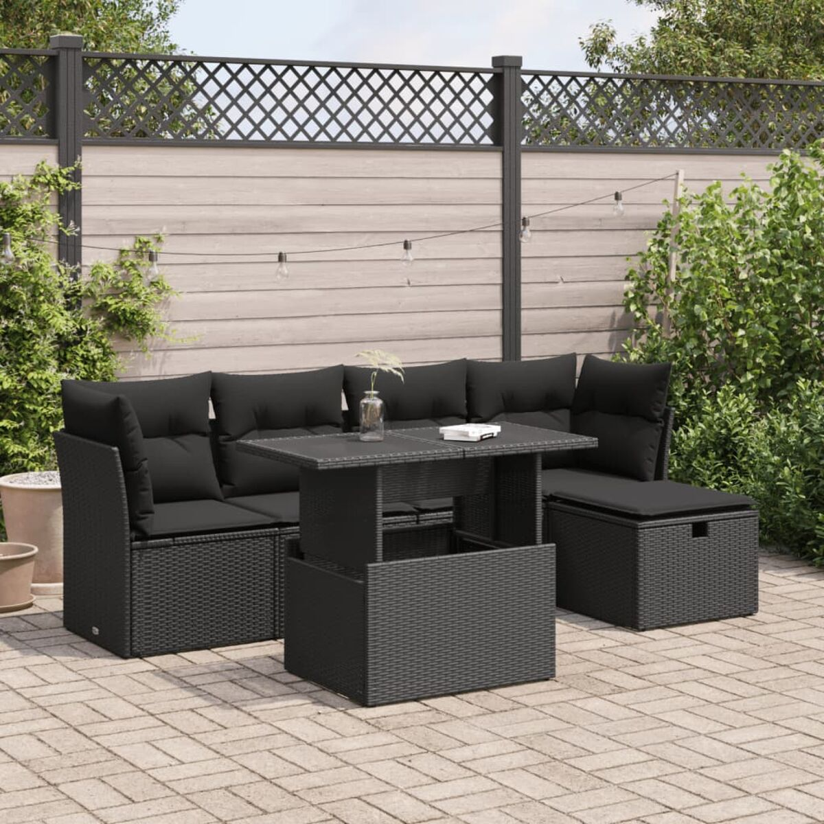 Divano componibile nero da esterno con tavolo abbinato. Su un patio pavimentato con recinzione e piante sullo sfondo.