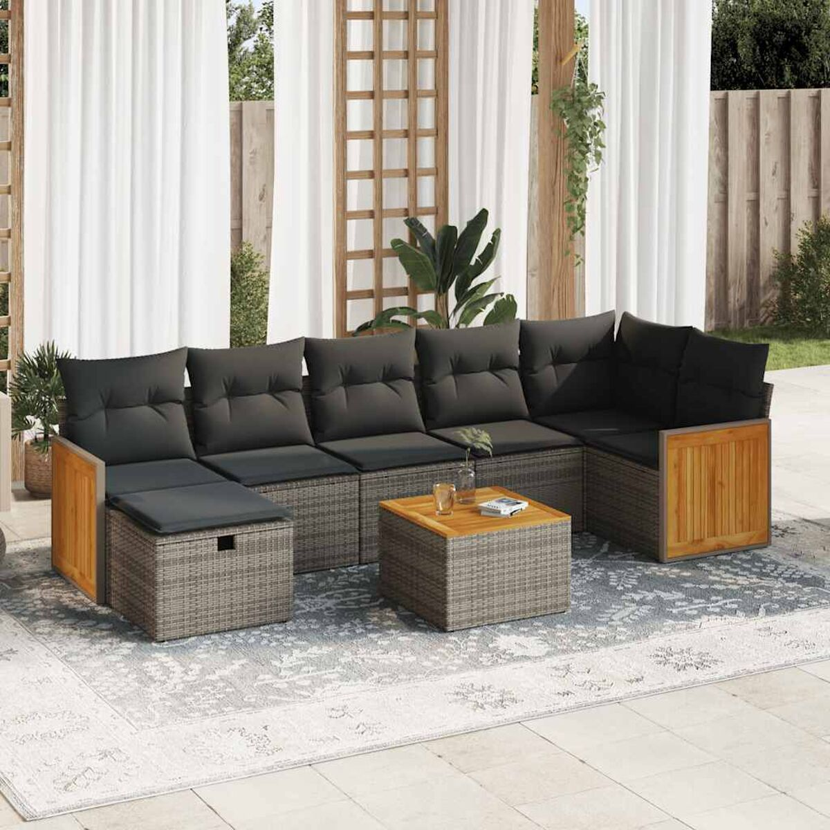 Terrassenmöbelset aus grauem Rattan, Holzverkleidung und schwarzen Kissen auf einem gemusterten Teppich.