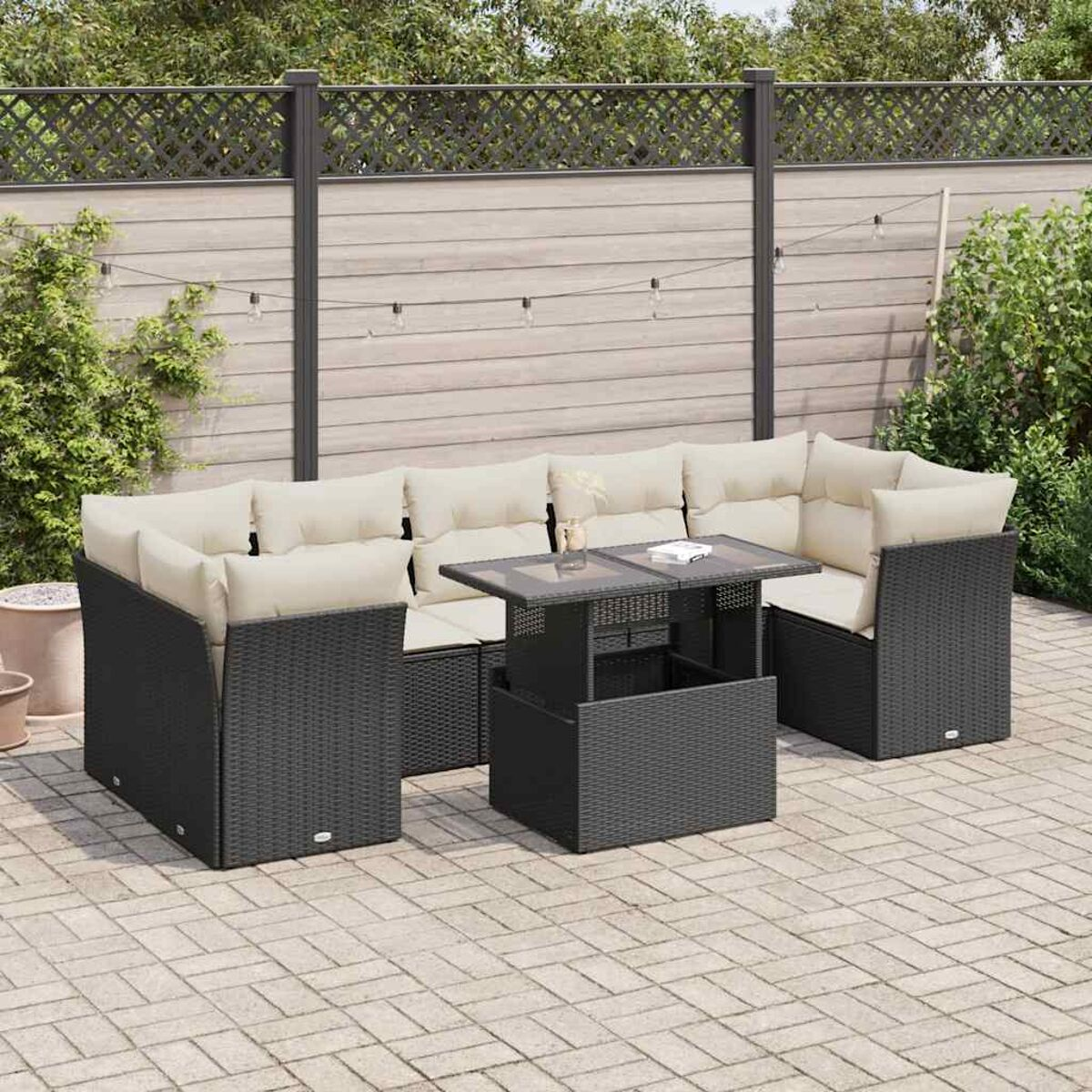 Divano componibile da esterno in rattan nero con tavolo in vetro. Recinzione in legno sullo sfondo.