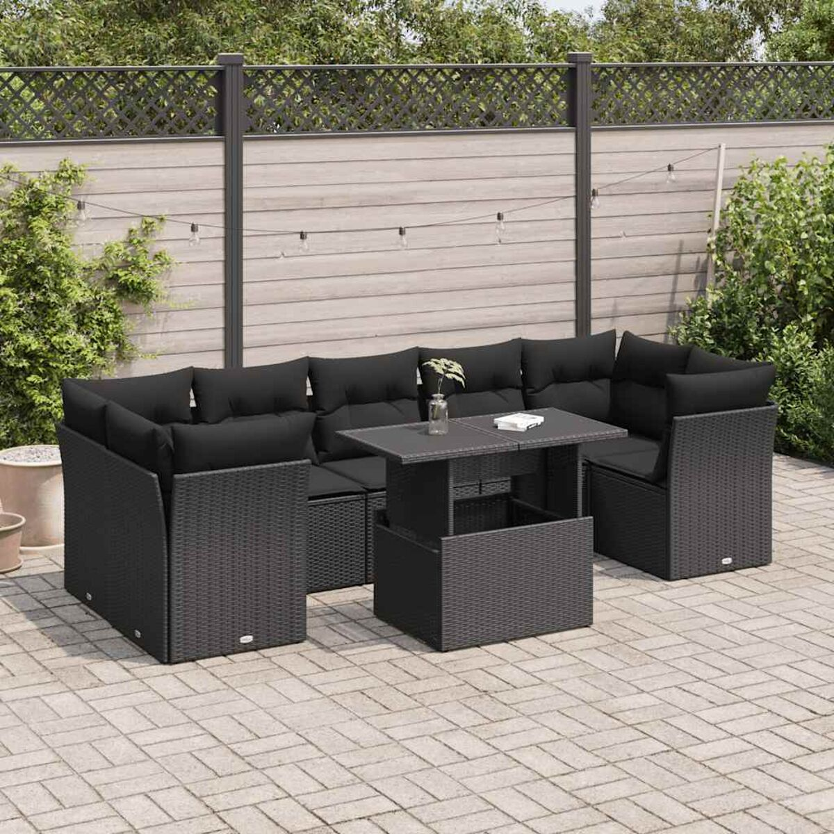 Set di mobili da esterno in rattan nero con tavolo e sedute, cuscini neri.