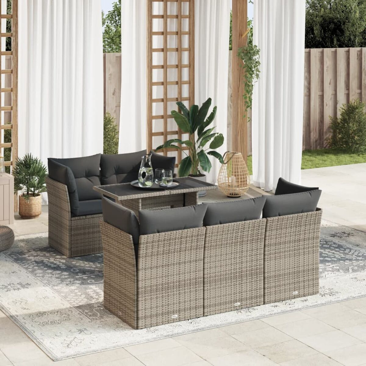 Set divano in vimini beige con cuscini grigi, tavolo e piante.