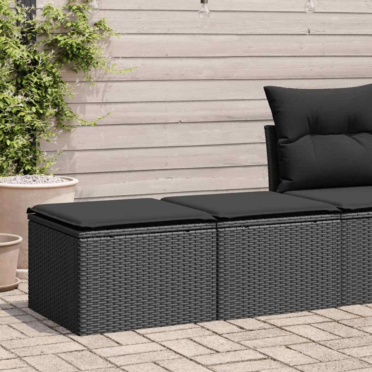 Divano componibile nero da esterno con cuscini su un patio in mattoni.