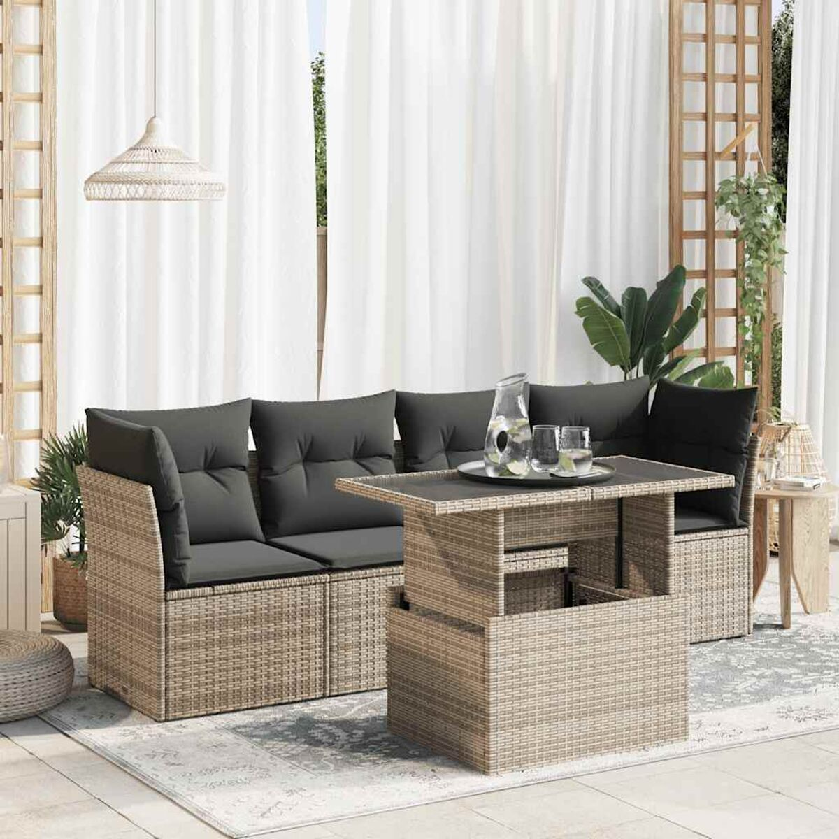 Set divano in rattan con cuscini e tavolo. Scena con tende, brocca e bicchieri.