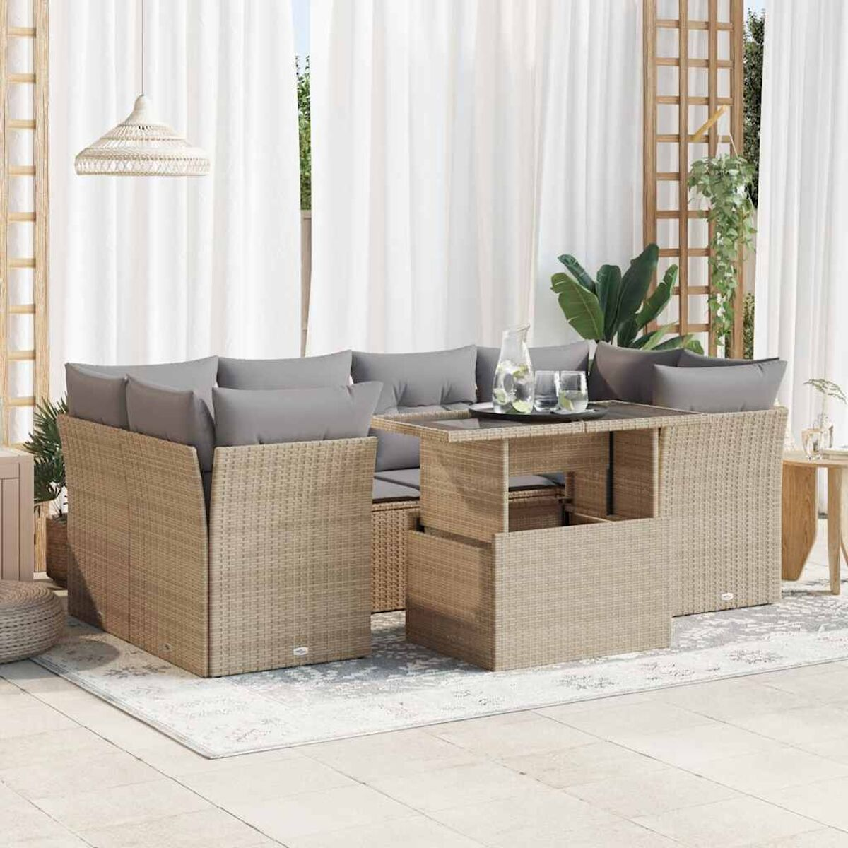 Divano in rattan da esterno con cuscini grigi, tavolo in vetro e tende bianche sullo sfondo.