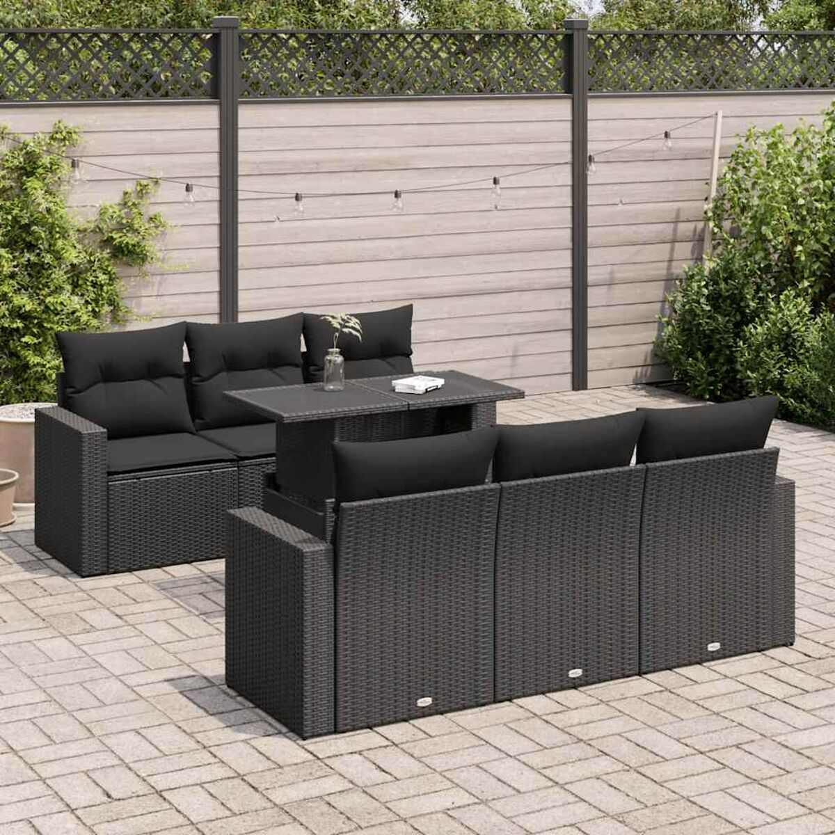 Divano angolare da esterno in rattan nero con tavolo e cuscini neri su un patio in mattoni.