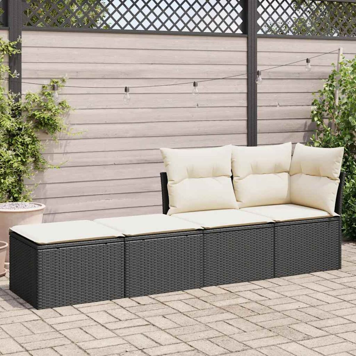 Set divano in rattan con cuscini color crema. Lo sfondo include una recinzione decorativa e piante.