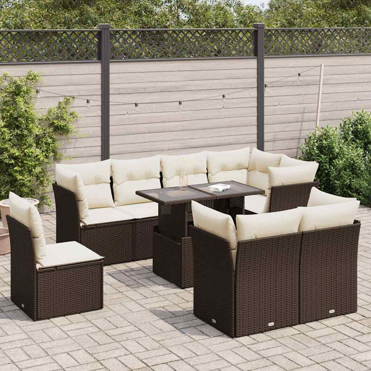 Outdoor-Terrassenset mit Sofa, Tisch und Stühlen. Braune Korbmöbel, weiße Kissen. Gartenkulisse.