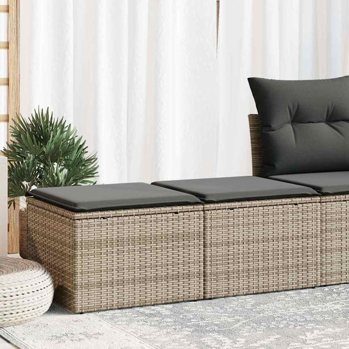 Beiges Outdoor-Sofa mit grauen Kissen. Weiße Vorhänge und ein Teppich im Hintergrund. Eine Pflanze an der Seite.
