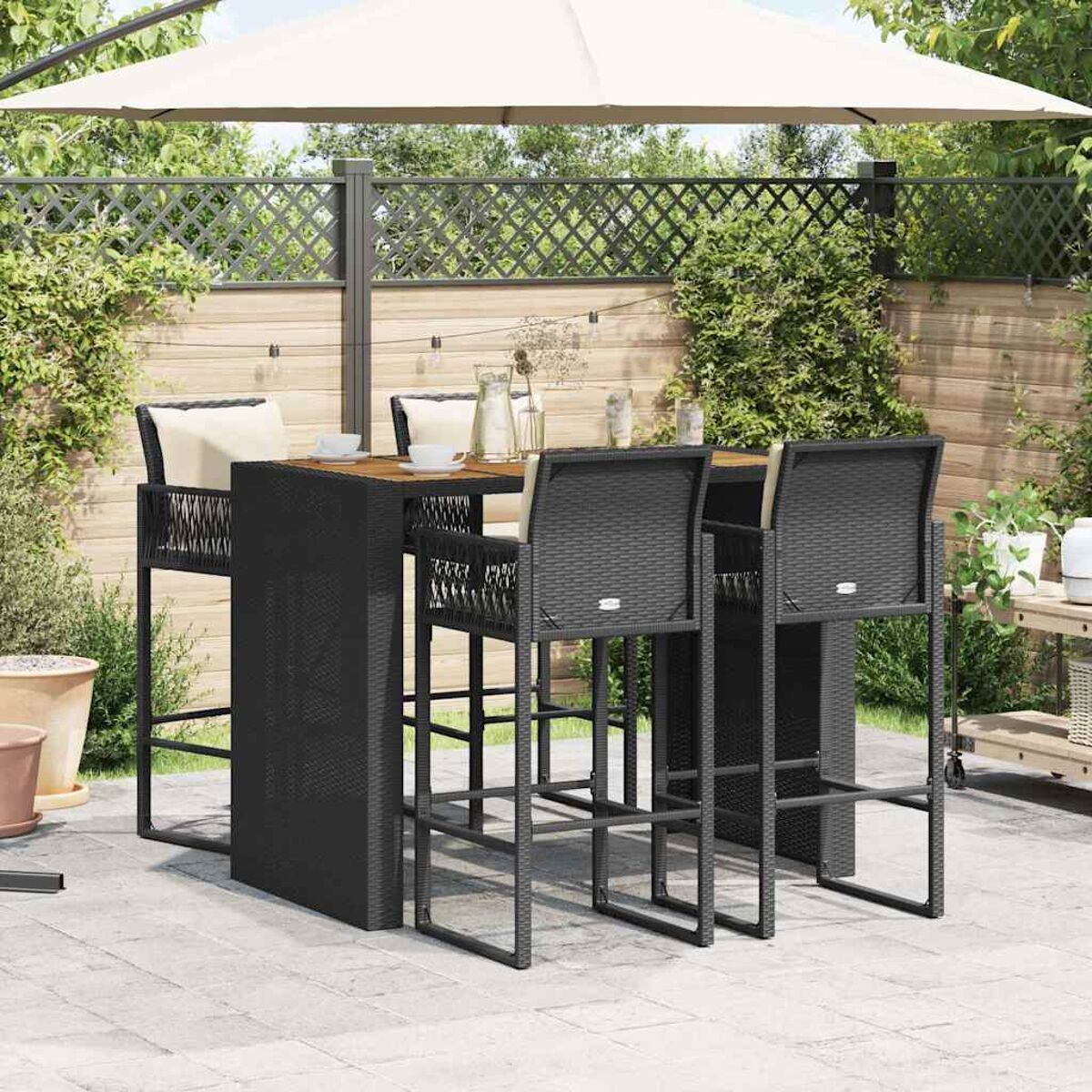 Bartisch und Barhocker im Freien auf einer Terrasse, mit Sonnenschirm und Gitterzaun.