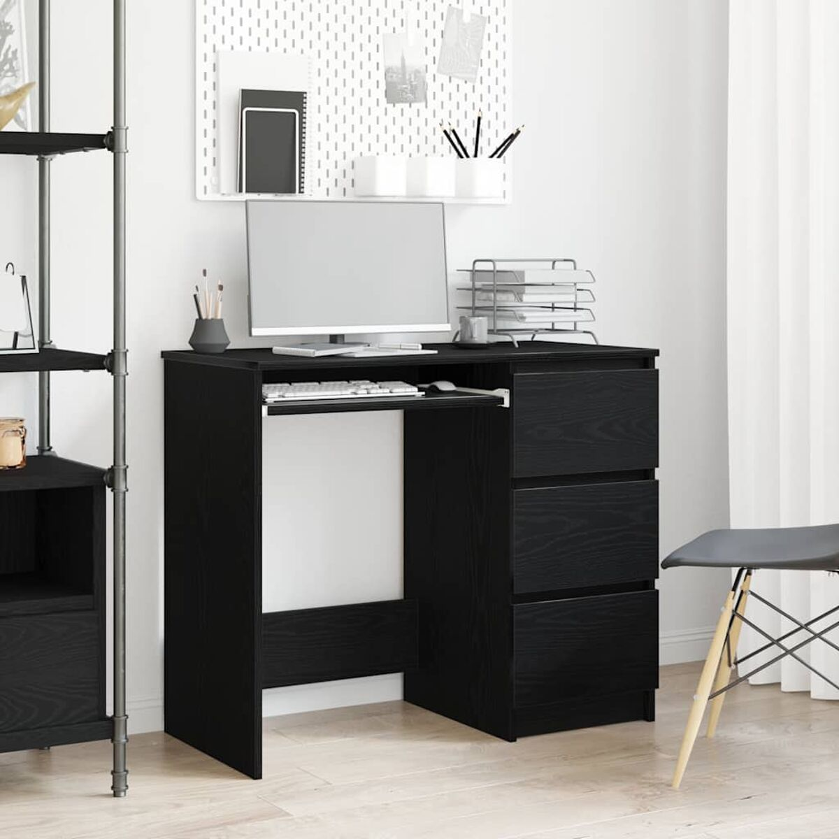 Schwarzer Schreibtisch mit Schubladen, Computer und Zubehör vor weißer Wand.