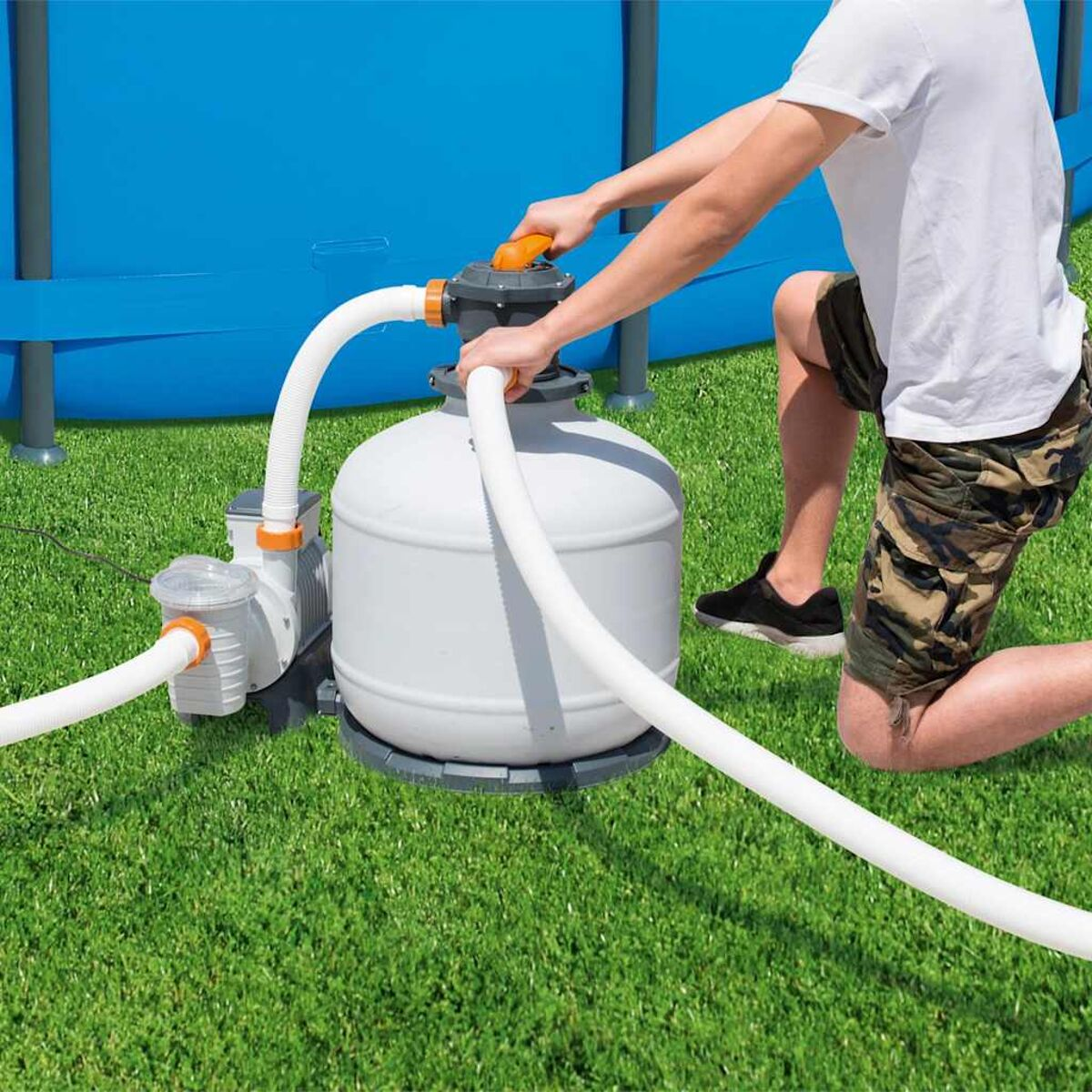 Eine Person kniet in der Nähe eines Poolpumpen- und Filtersystems, mit angeschlossenen Schläuchen.