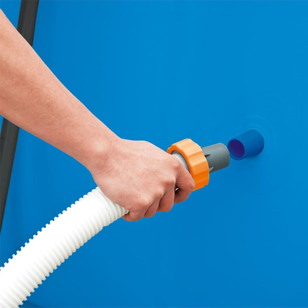 Hand hält einen Schlauch, um ihn an einen blauen Pool anzuschließen. Orangefarbene und graue Anschlüsse.