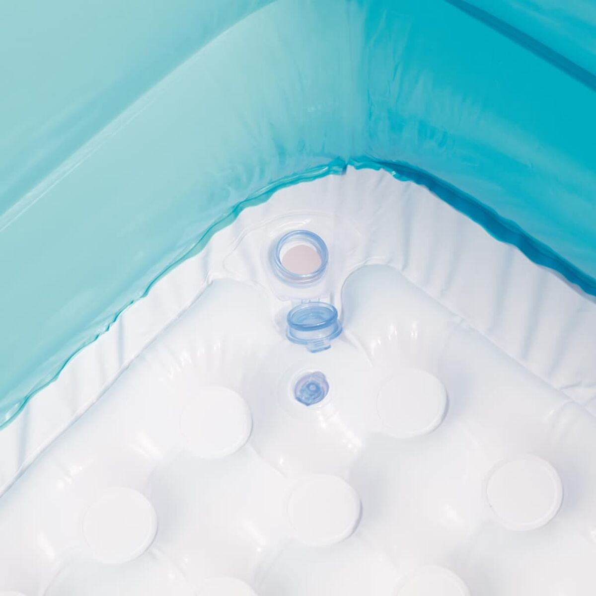 Gros plan de l'intérieur d'une piscine gonflable blanche. Une entrée d'eau est visible. Eau bleue.