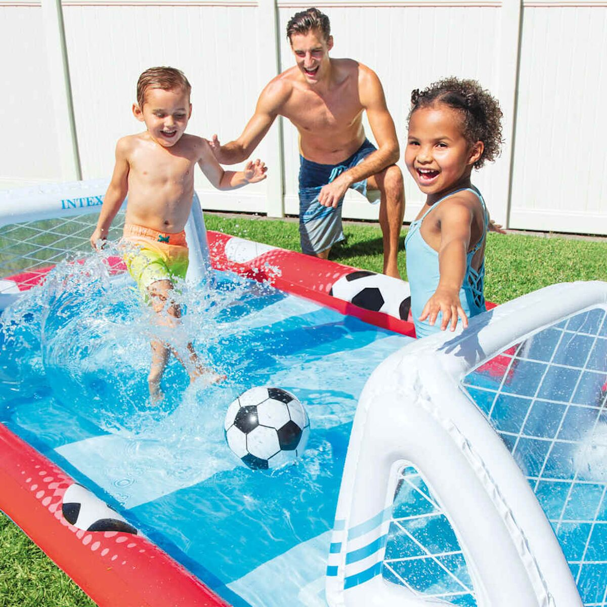 Bambini e un uomo giocano in una piscina gonfiabile di calcio blu e rossa. Un pallone da calcio è nell'acqua.