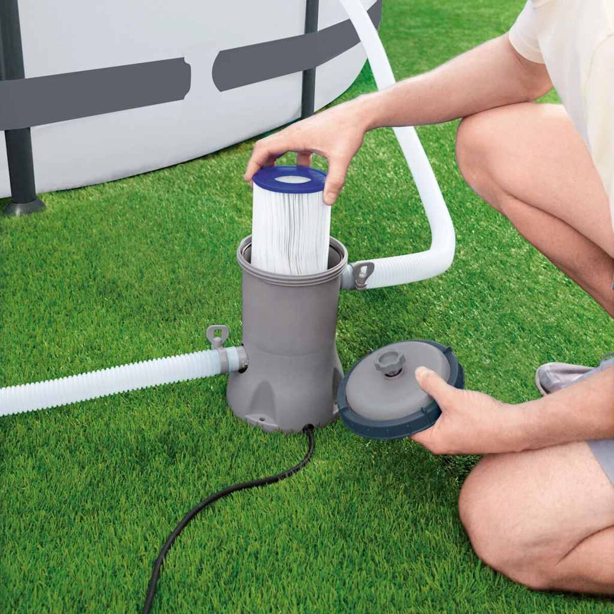 Person installiert einen Poolfilter. Der Filter ist zylindrisch und blau. Grünes Gras im Hintergrund.