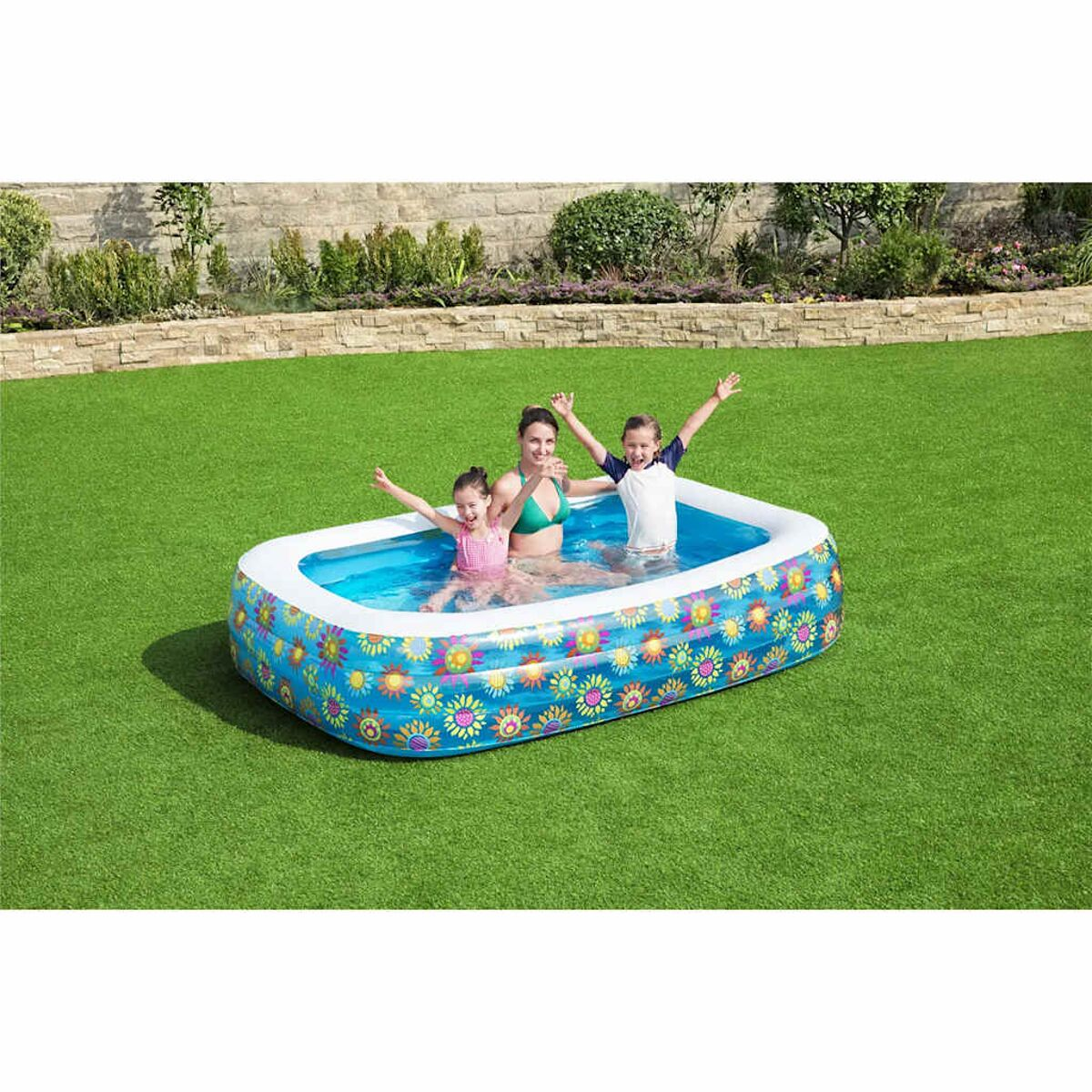 Drei Kinder und eine Frau in einem blauen aufblasbaren Pool auf grünem Gras, heben Arme.