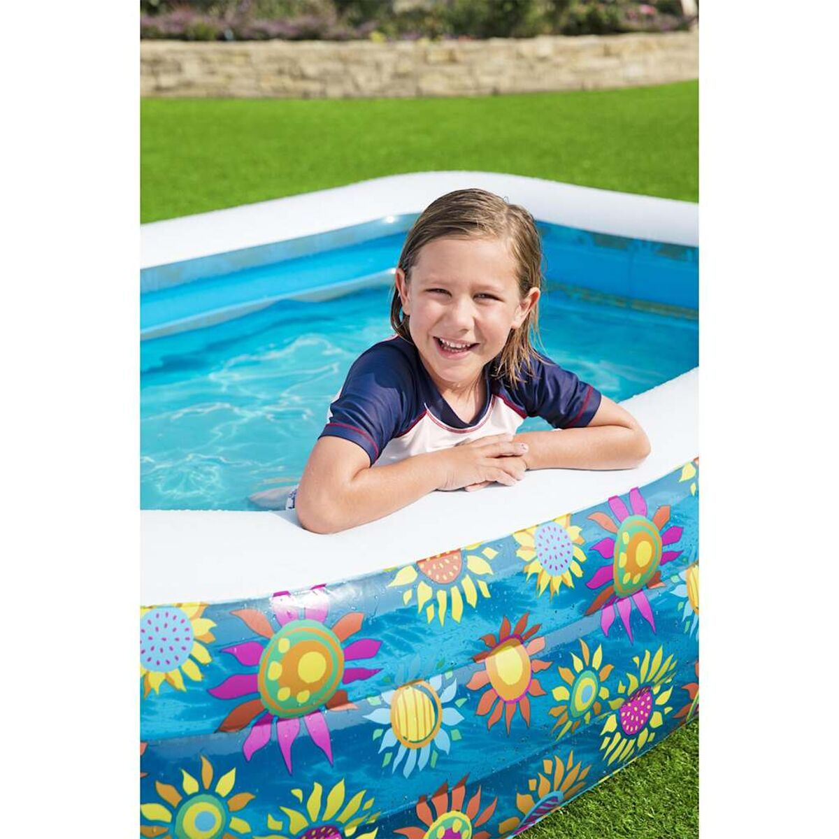 Ein junges Mädchen lächelt in einem blau-weißen Pool mit Blumendekorationen.