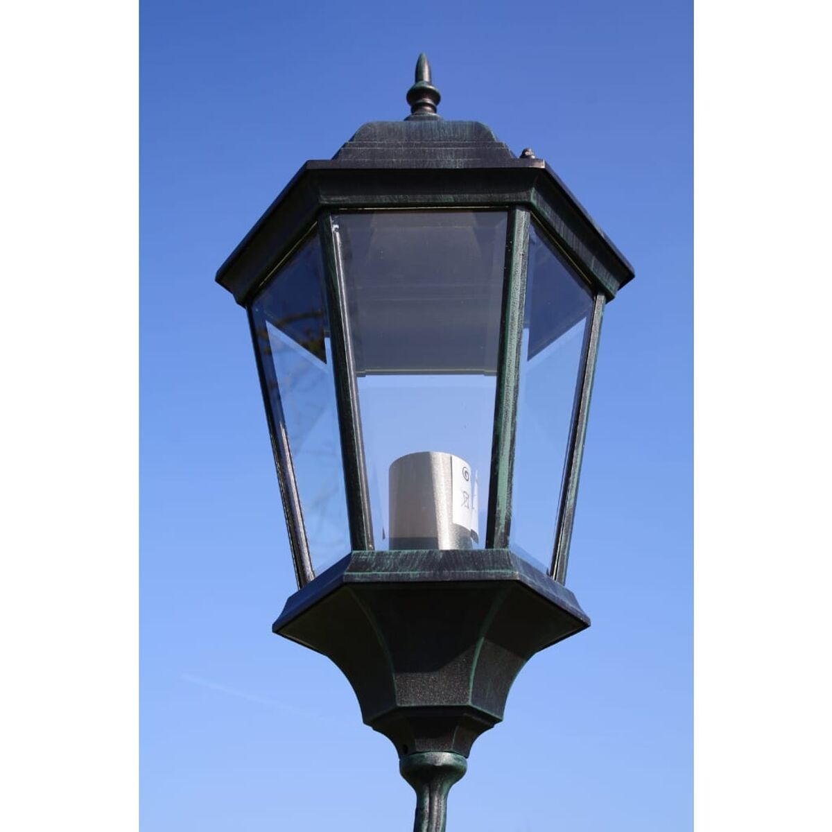 Schwarze Außenlaterne mit Glasscheiben und blauem Himmel im Hintergrund.