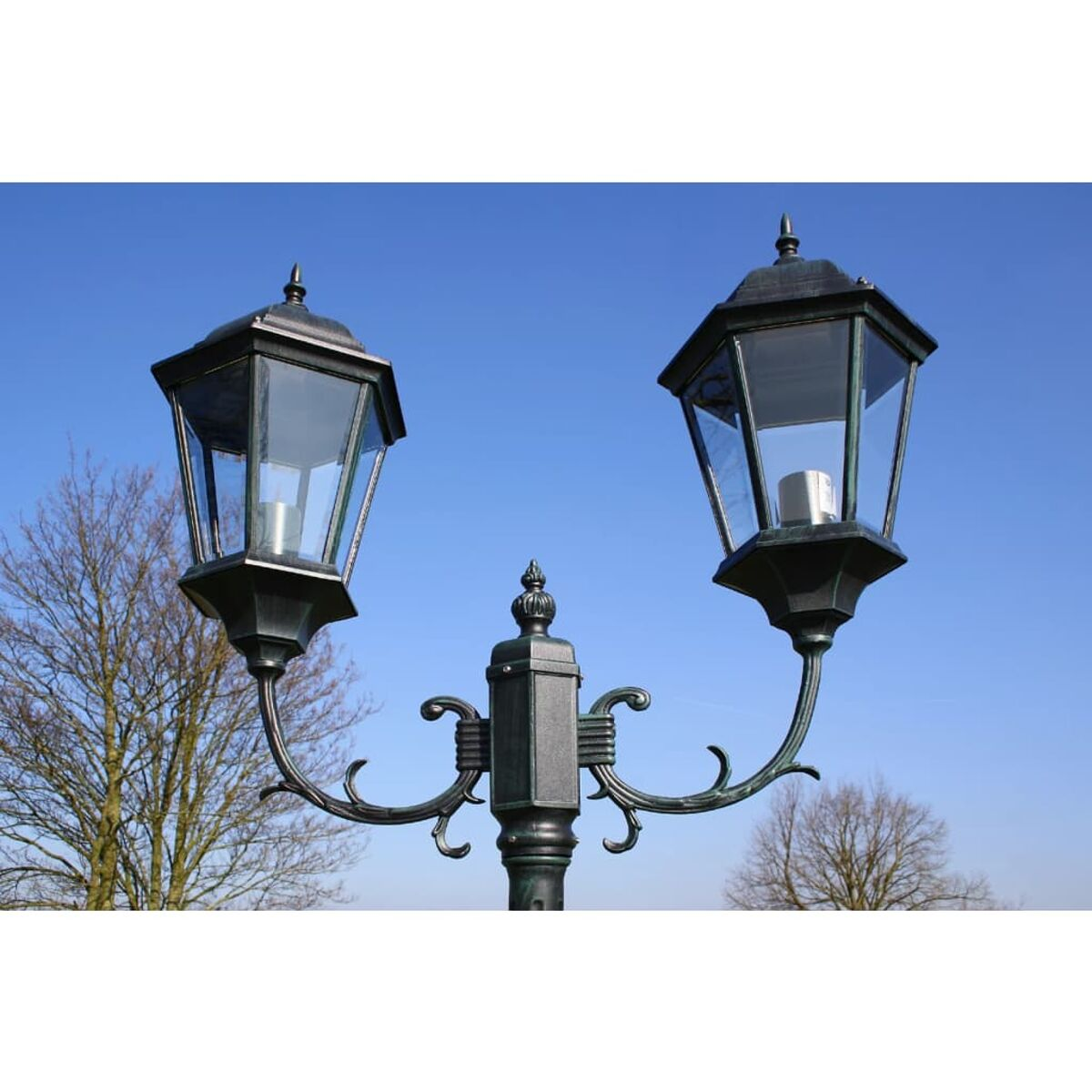 Zwei schwarze Vintage-Straßenlaternen mit blauem Himmel im Hintergrund.