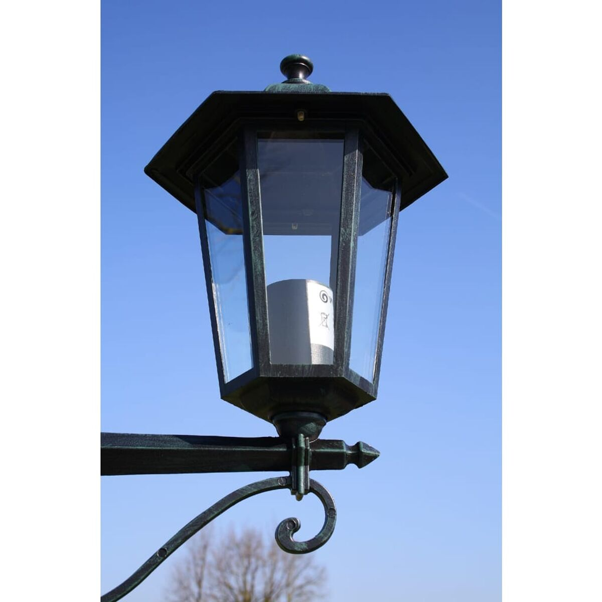 Schwarze Außenlaterne mit klaren Glasscheiben. Hat eine dekorative Oberseite und ist an einer Stange befestigt.