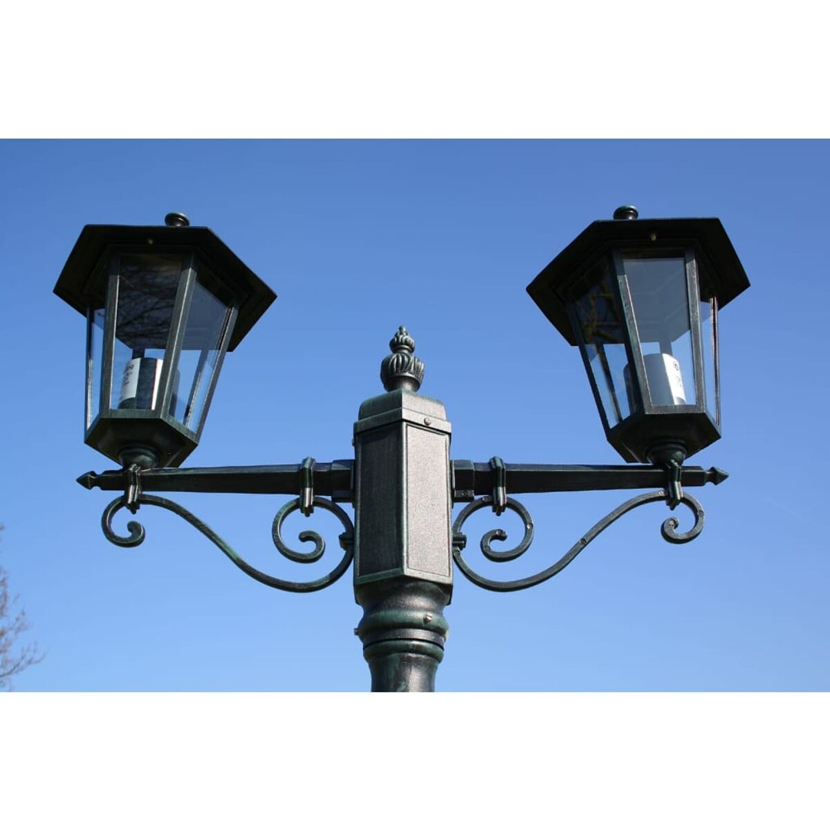 Zweiköpfige schwarze Straßenlaterne mit Glasscheiben vor blauem Himmel.