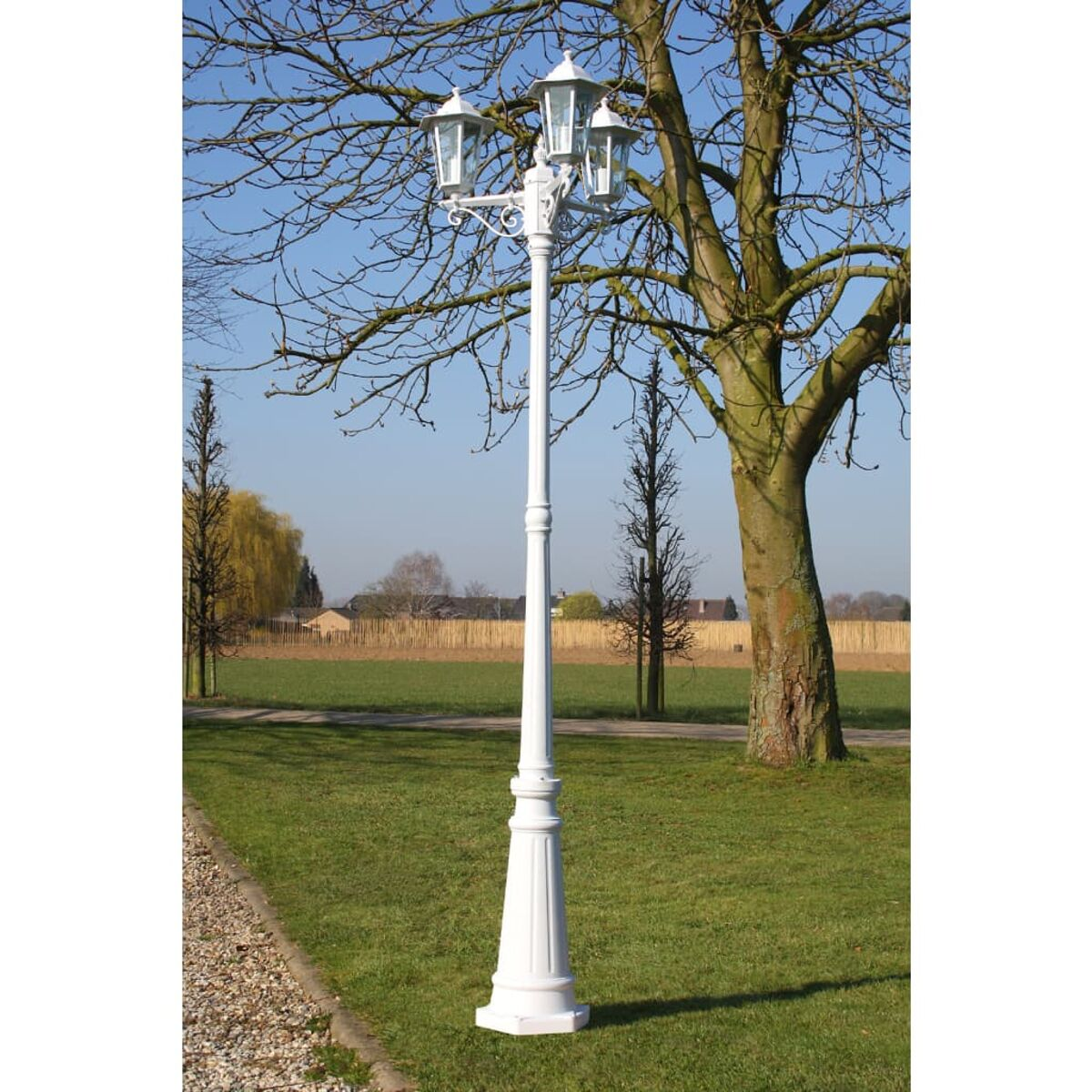 Weiße Straßenlaterne mit drei Lichtern in einem Park. Die Lampe hat verzierte Details.