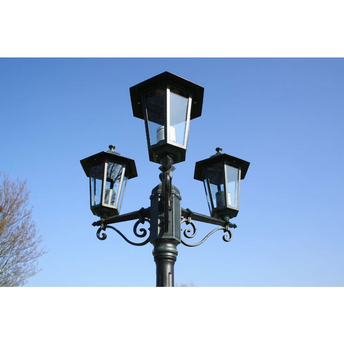 Laternenpfahl mit drei Lampen. Schwarzes Metall. Klarer blauer Himmel im Hintergrund.