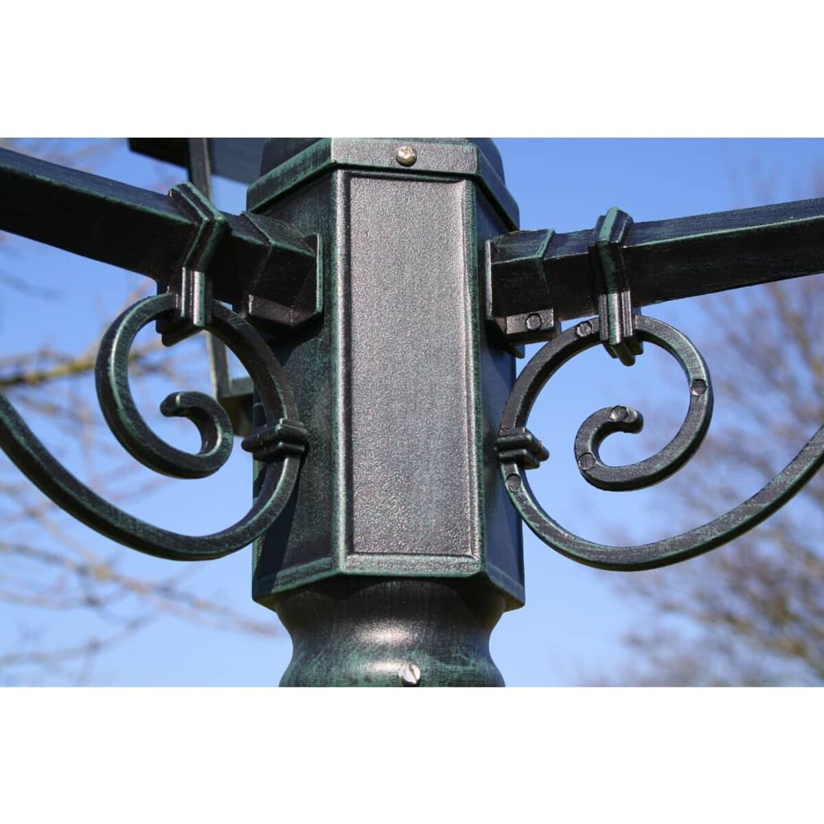Dekorativer Metallpfosten mit Schnörkeln. Der Pfosten ist dunkelgrün mit hellem blauem Himmel.