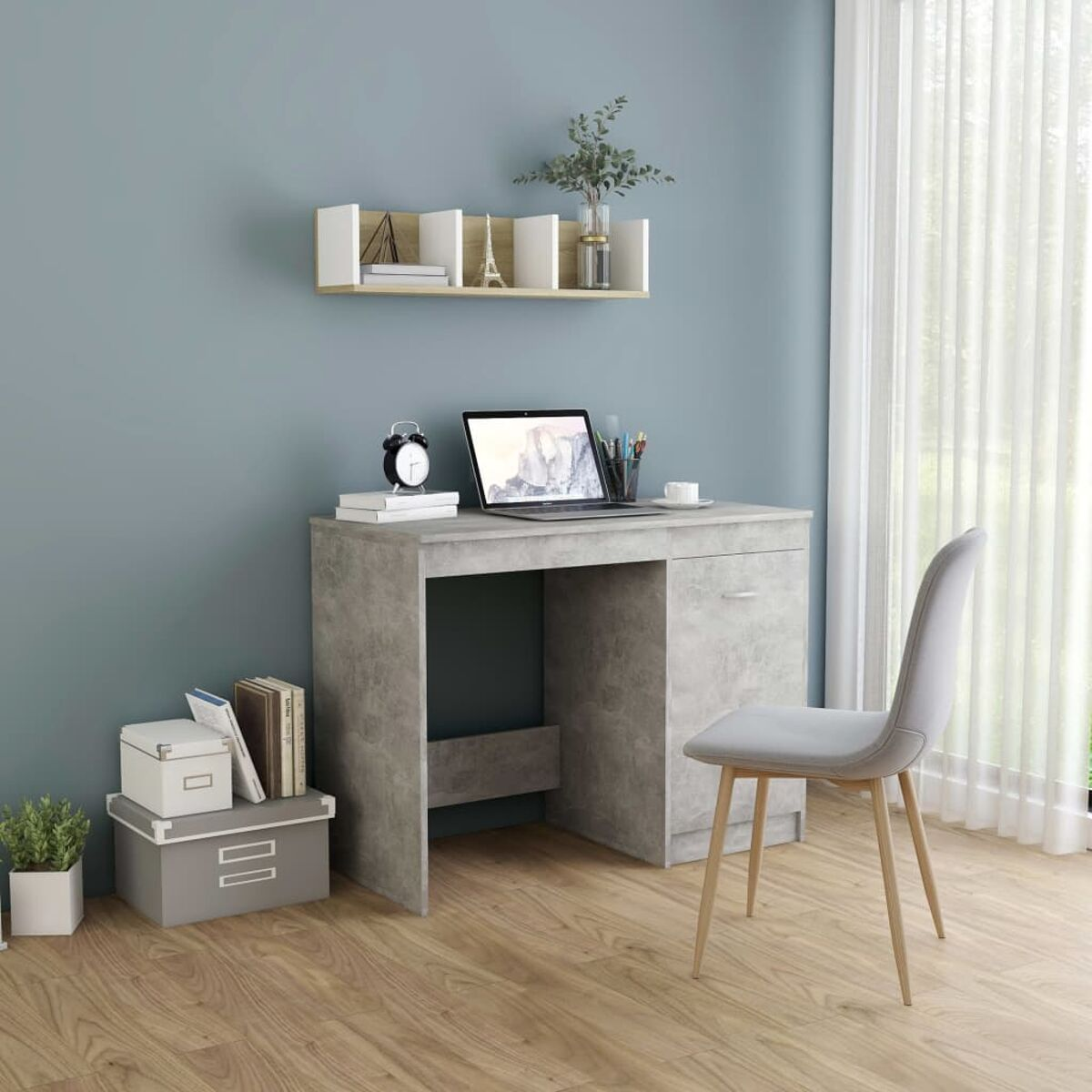 Grauer Schreibtisch mit Laptop, Büchern und Stuhl. Ein Regal mit Deko befindet sich darüber.