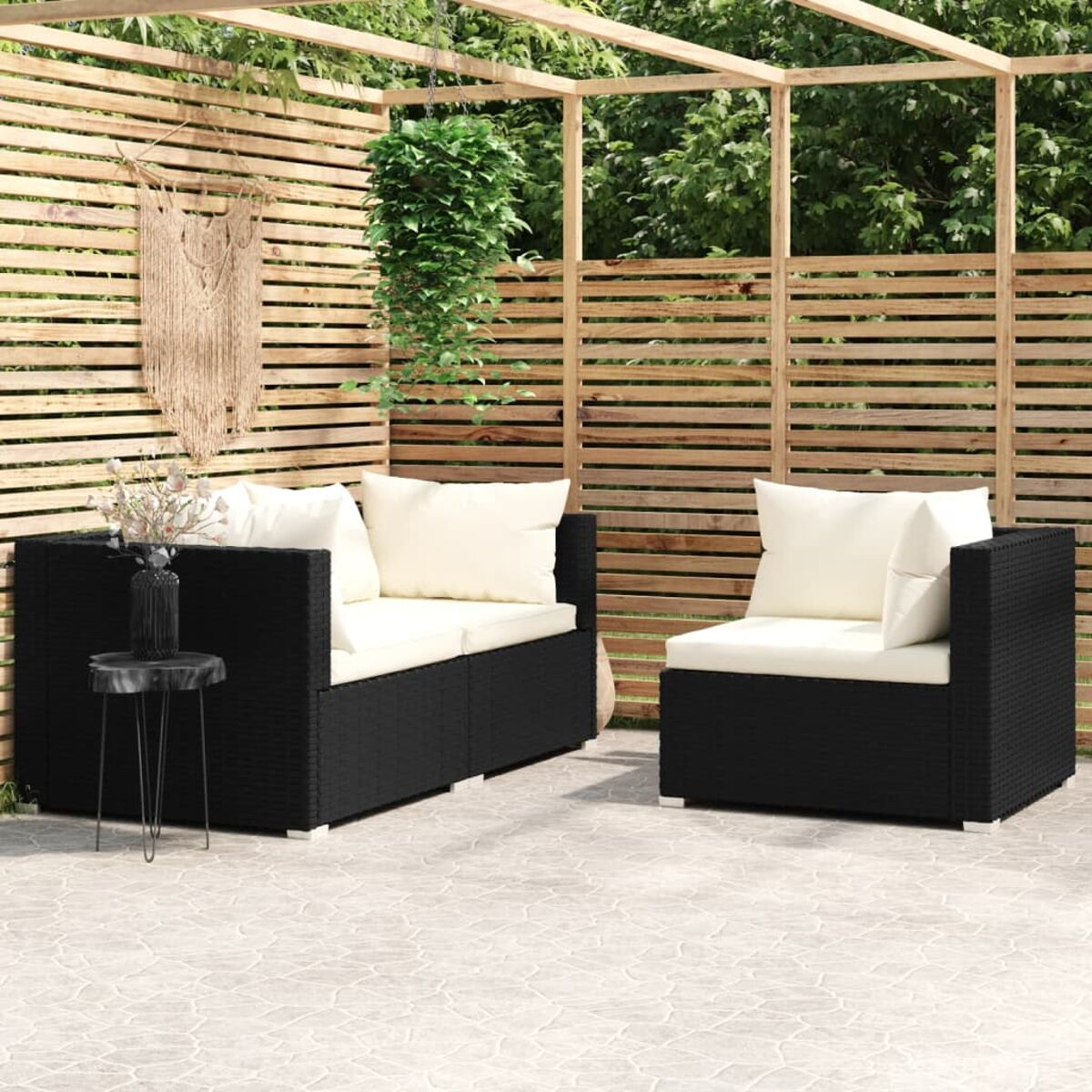 Schwarzes Rattan-Gartenmöbelset mit weißen Kissen. Holzzaun und Pergola im Hintergrund.