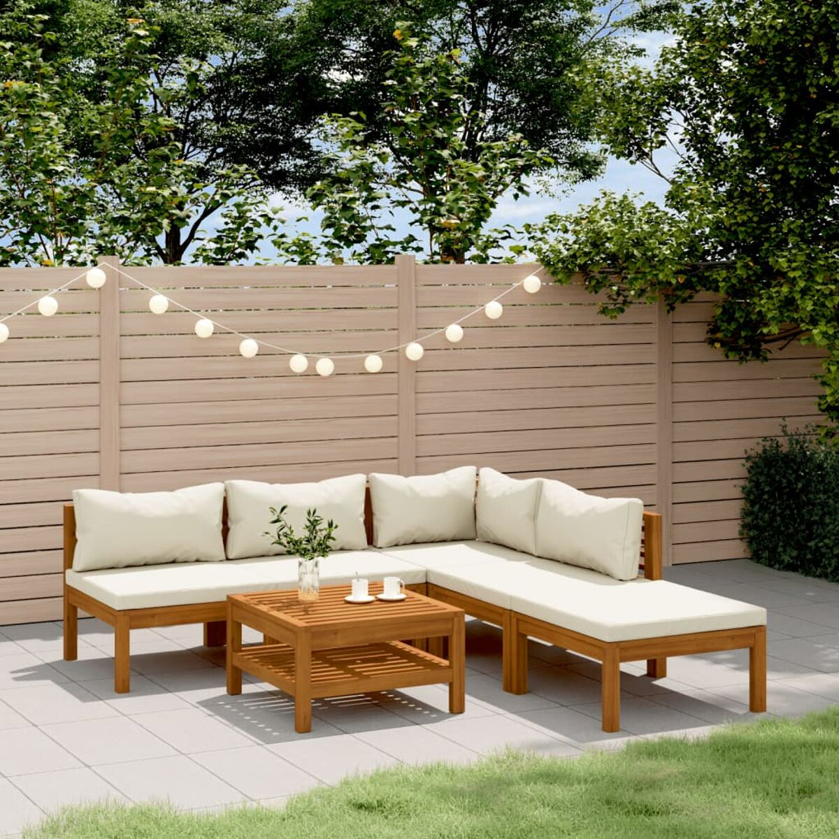 Garnitur für den Außenbereich: Ecksofa aus Holz, Couchtisch mit zwei Tassen und Lichterketten über Rasen.