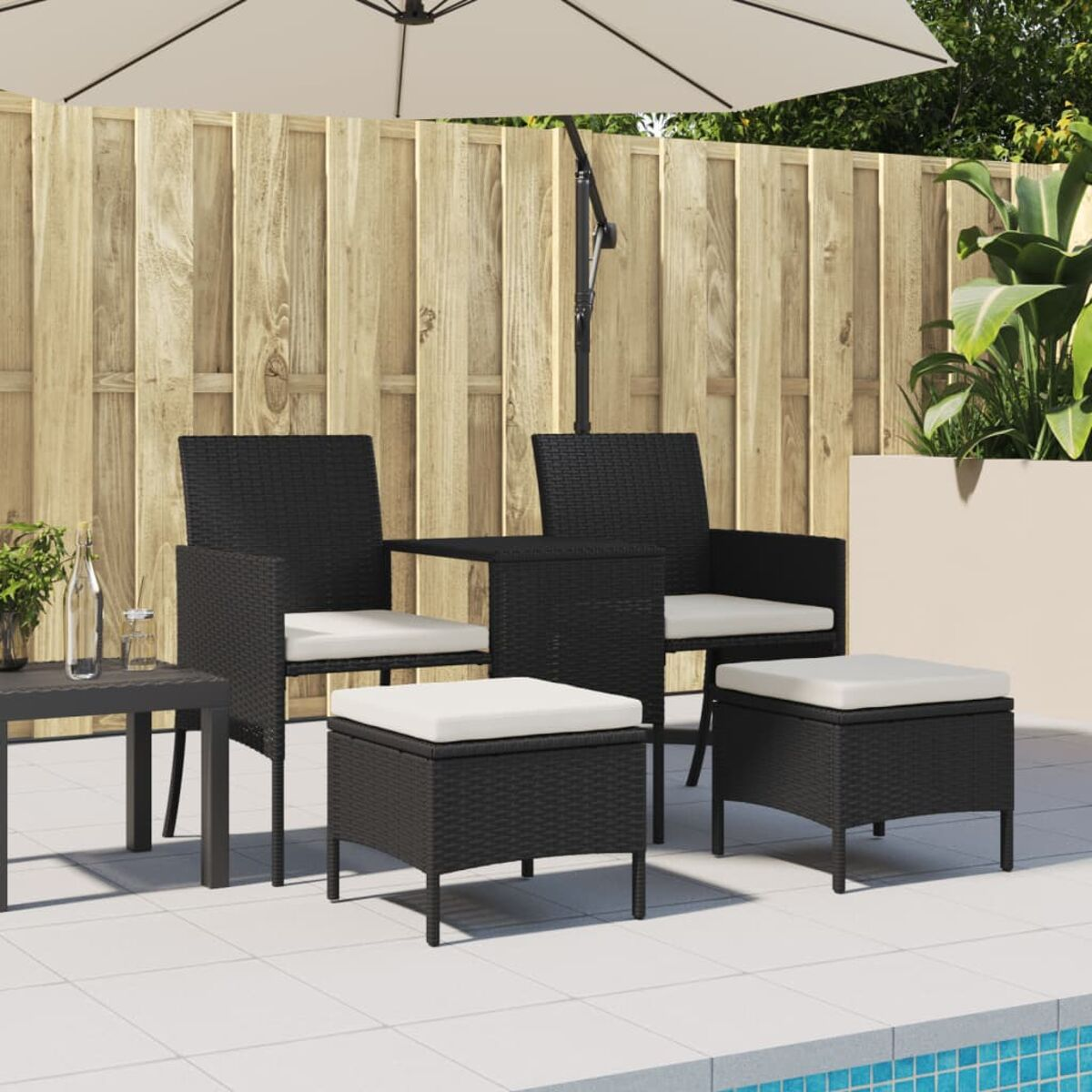 Set da patio esterno con sedie nere, tavolo e pouf; ombrellone e staccionata in legno.
